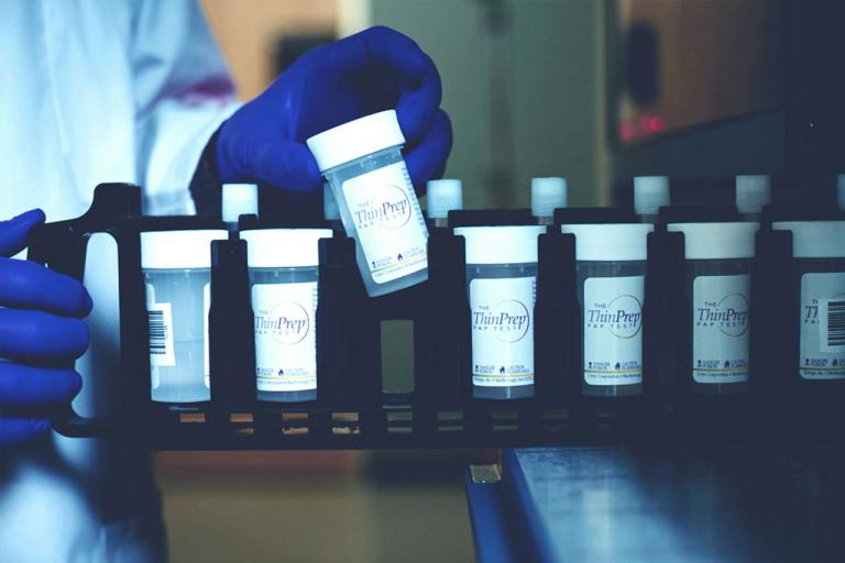 Behandschuhte Hand bei der Eingabe eines Fläschchens in ein Tray